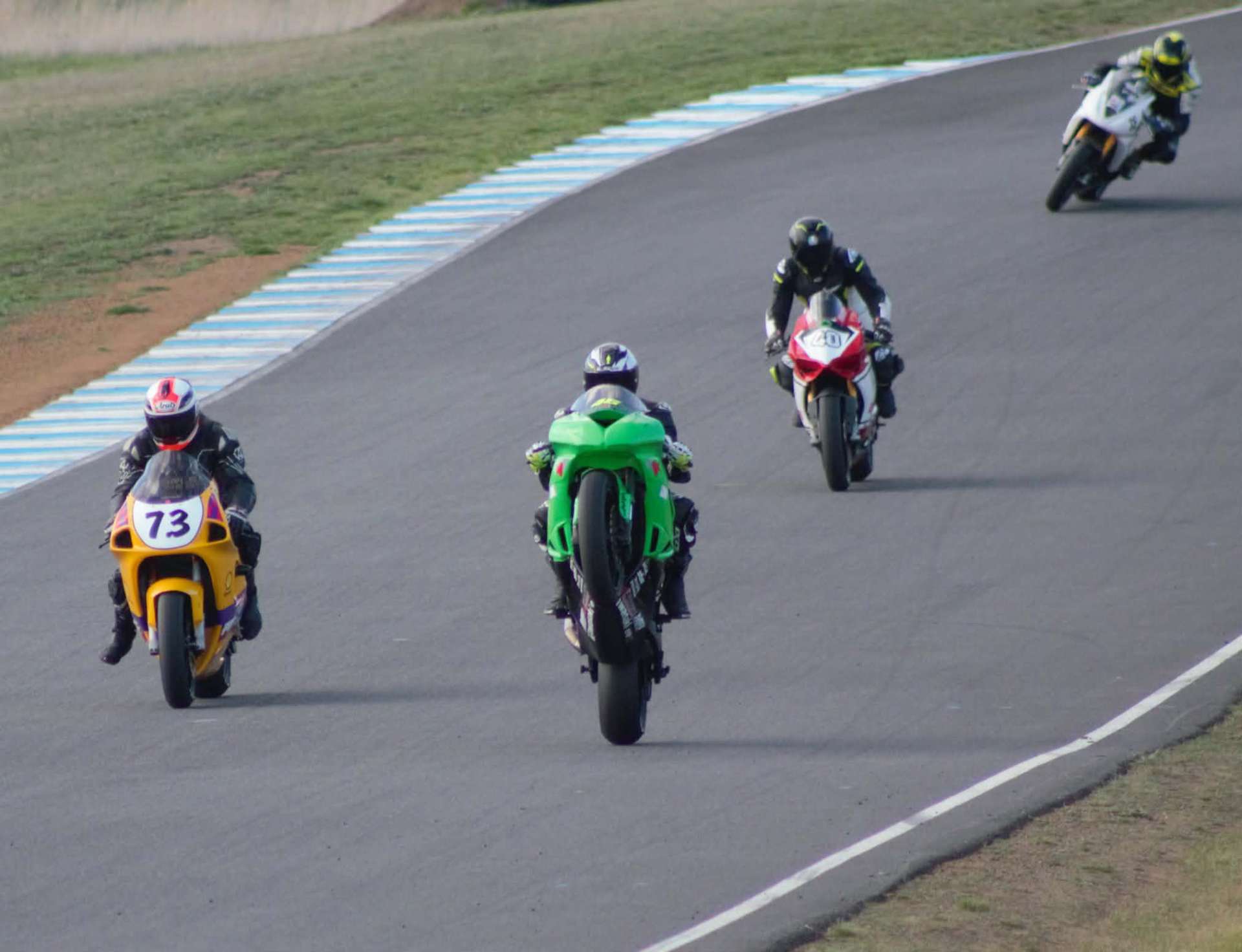Pack of riders exiting a corner, front wheels lifting